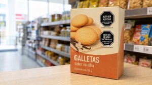 Caja de galletas en un anaquel de supermercado con dos octógonos negros de advertencia, ALTO EN AZÚCAR y ALTO EN GRASAS SATURADAS, en la esquina superior derecha